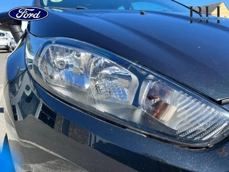 Gros plan sur le phare avant gauche d'une Ford Fiesta noire de 2015, mettant en valeur les détails du bloc optique.