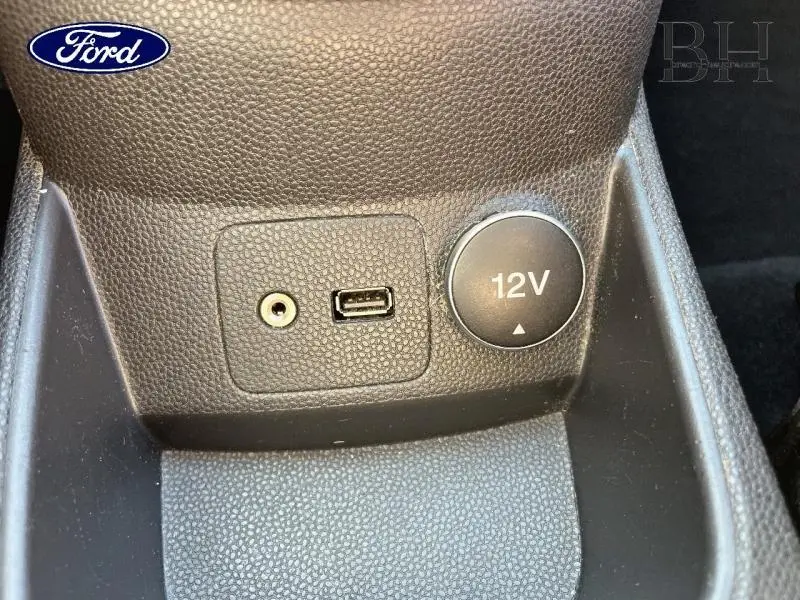 Détail de la console centrale noire de la Ford Fiesta 2015 montrant une prise 12V, un port USB et une entrée auxiliaire audio.