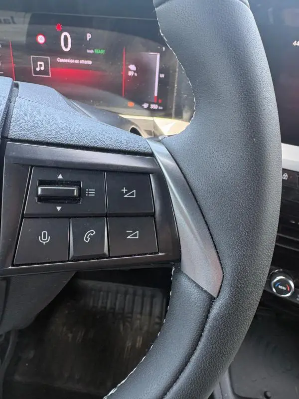Gros plan sur le volant côté gauche de l'Opel Mokka électrique gris 2025 avec commandes audio et tableau de bord numérique.