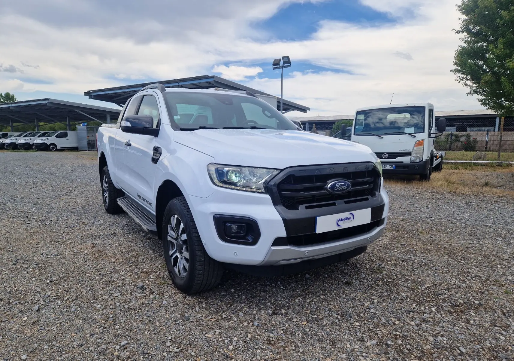 Ford Ranger Super Cabine blanc vu en 3/4 avant droit, avec calandre noire et marchepieds visibles.
