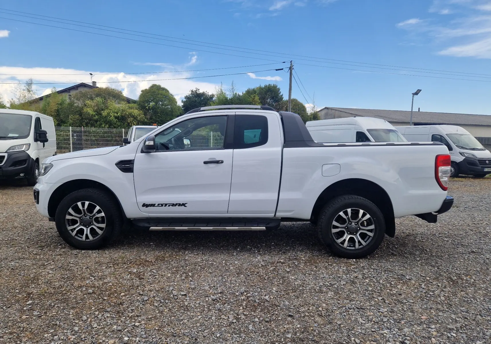 Vue de profil côté gauche d'un Ford Ranger Wildtrak blanc avec cabine allongée et marchepied visible.