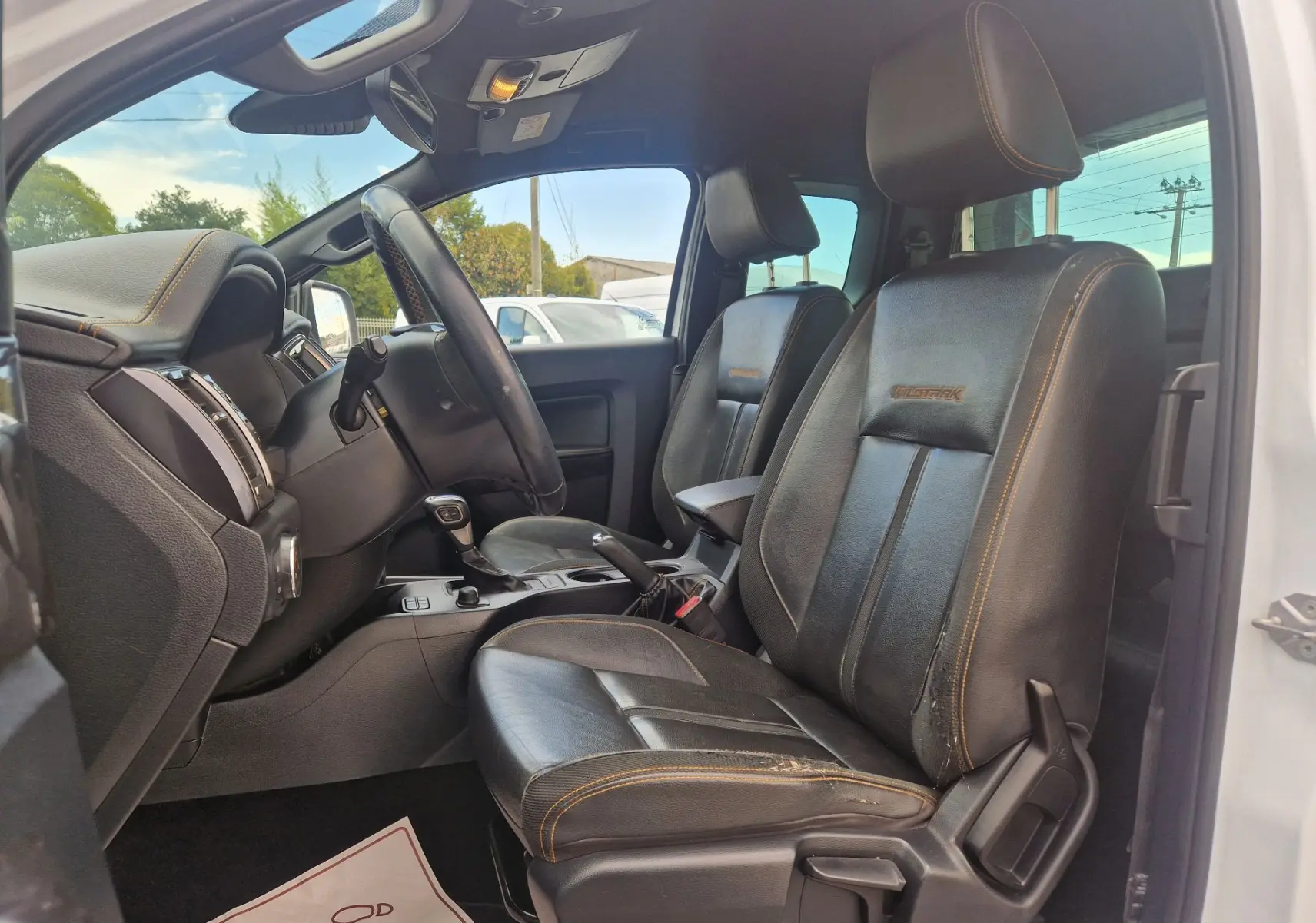 Intérieur côté conducteur du Ford Ranger Wildtrak 2020, sièges cuir noirs avec surpiqûres orange et logo Wildtrak brodé.