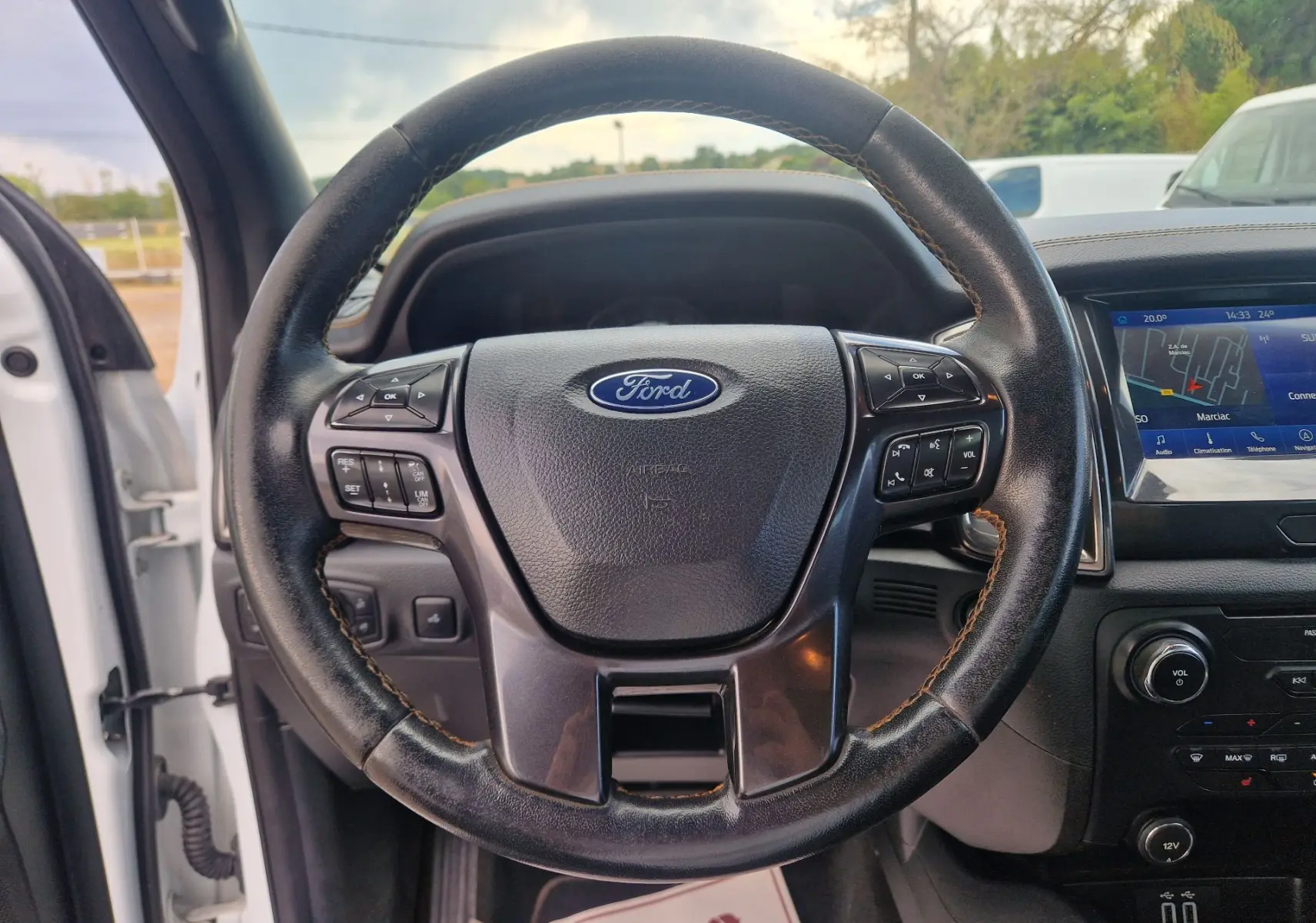 Vue intérieure centrée sur le volant en cuir noir du Ford Ranger Wildtrak blanc avec écran tactile et commandes au volant visibles.