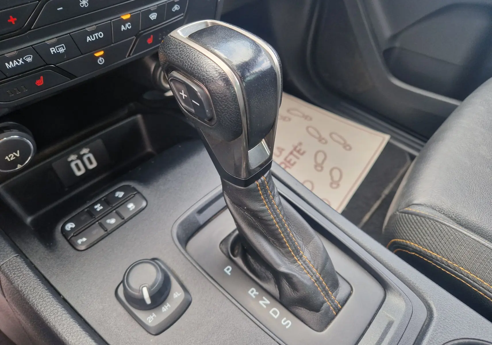 Gros plan sur le levier de vitesses automatique noir avec surpiqûres orange dans l’habitacle du Ford Ranger blanc.
