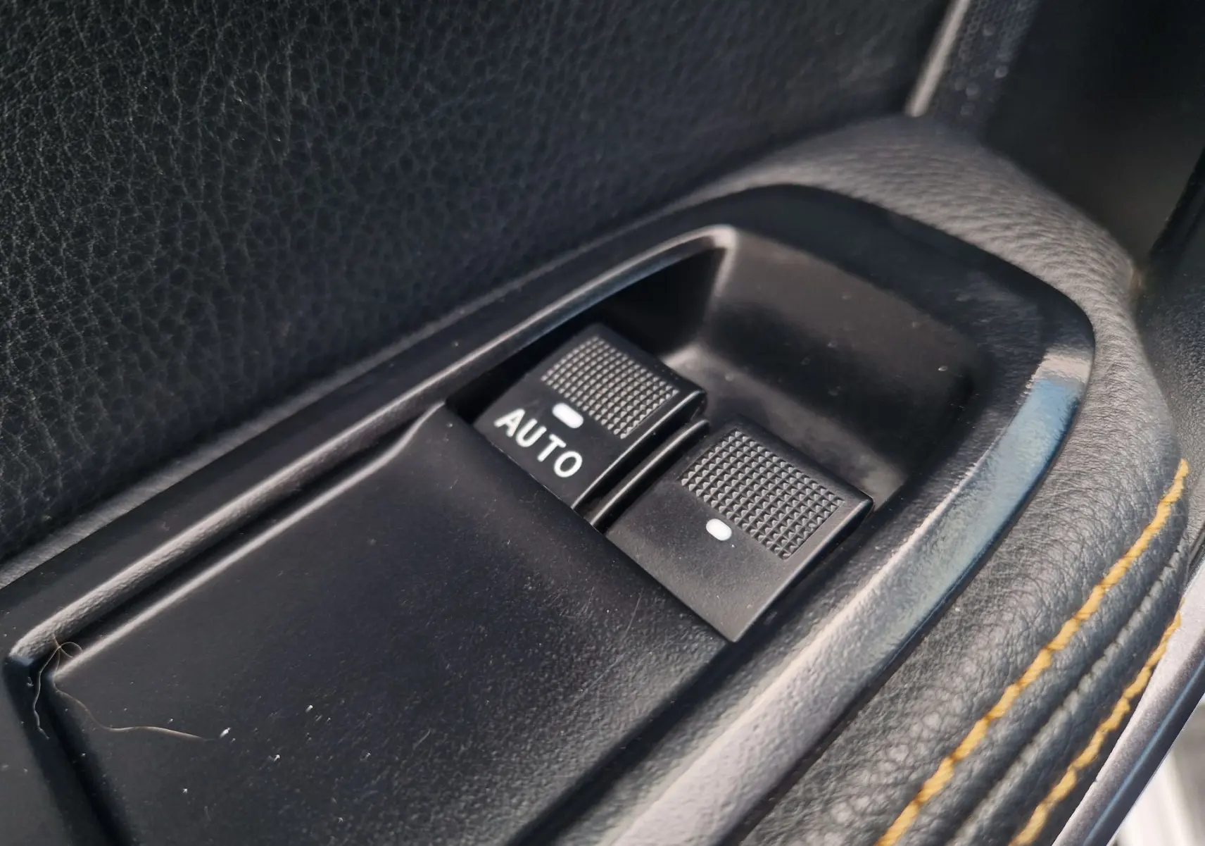Gros plan sur les commandes de lève-vitres en plastique noir avec surpiqûres jaunes sur la garniture intérieure du Ford Ranger blanc.