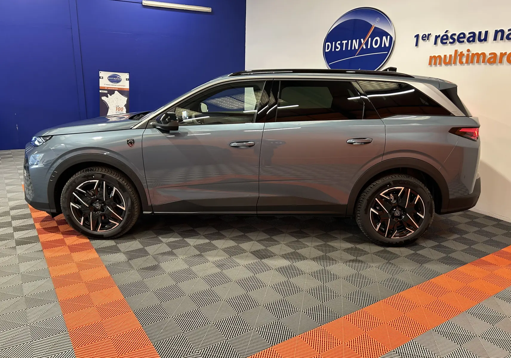 Vue de profil côté gauche d’un Peugeot 5008 bleu Ingaro avec jantes noires et toit ouvrant panoramique en intérieur showroom.