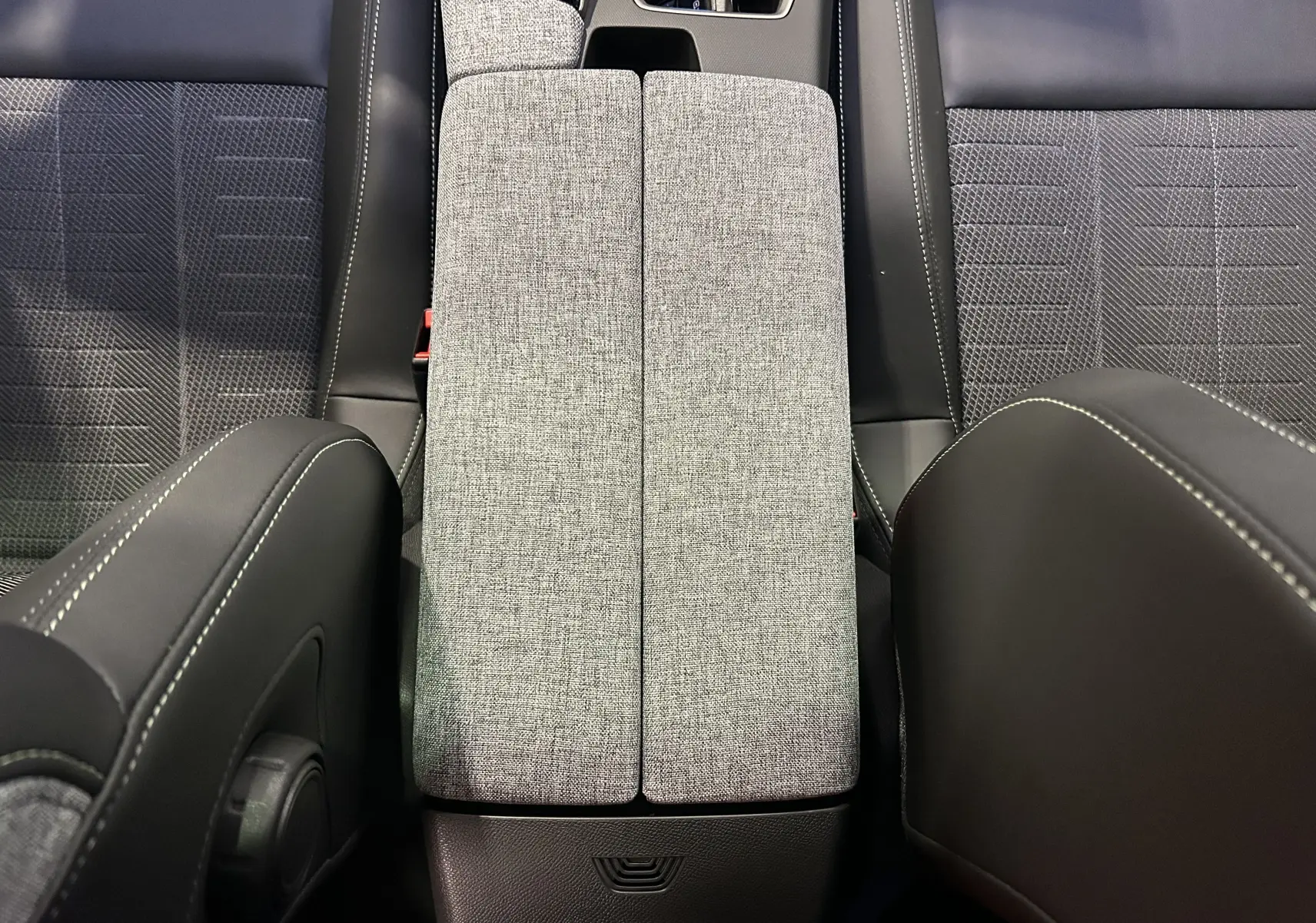 Vue plongeante sur l'accoudoir central tissu gris et sièges noirs avec surpiqûres blanches dans un Peugeot 5008 hybride 2026.