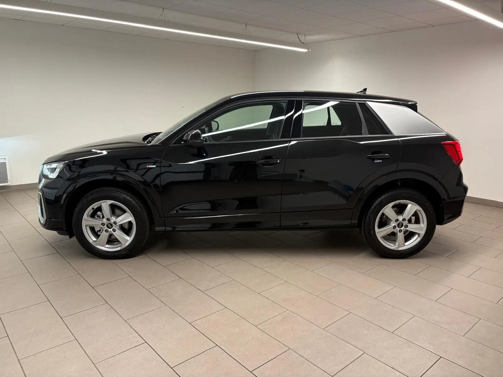 Profil côté gauche d'un Audi Q2 35 TFSI S Line noir mythic métallisé, intérieur clair, en showroom.