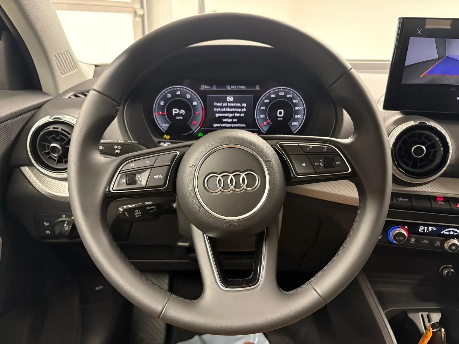 Vue rapprochée du volant multifonction noir de l'Audi Q2 35 TFSI S Line avec tableau de bord numérique allumé.