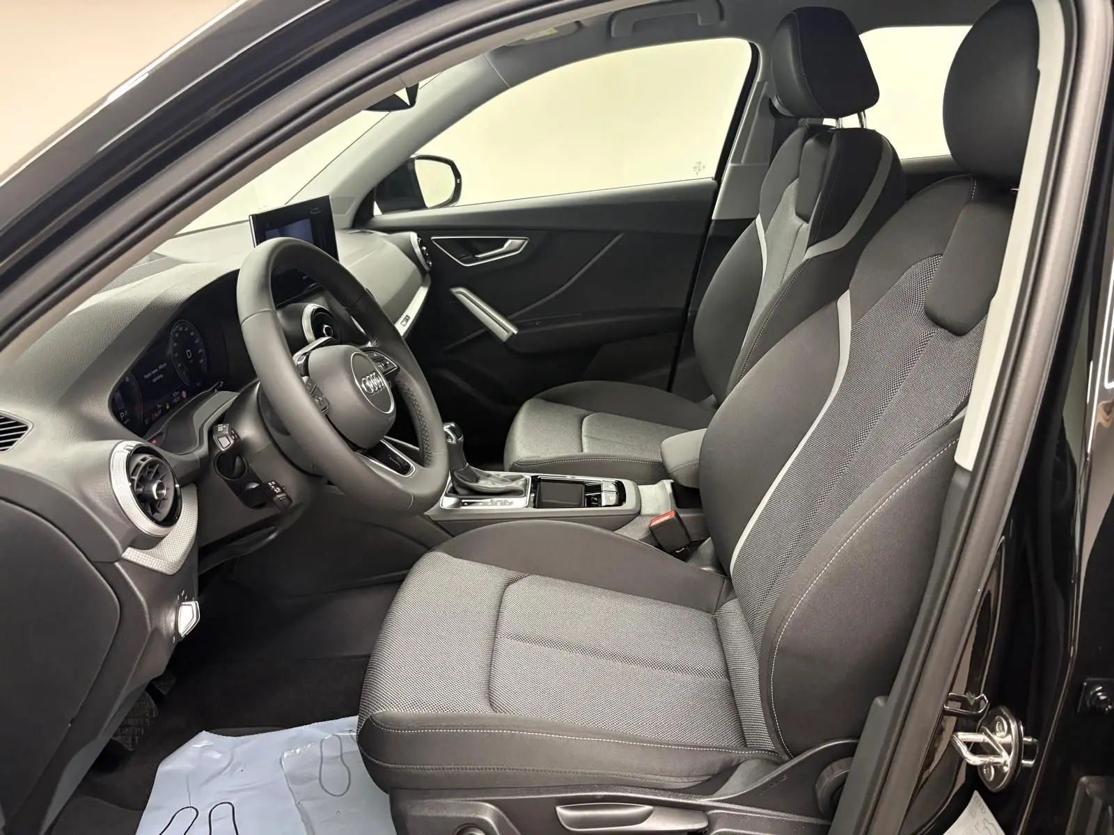 Vue intérieure côté gauche de l'Audi Q2 35 TFSI S Line 2026 avec sièges tissu gris et tableau de bord noir.