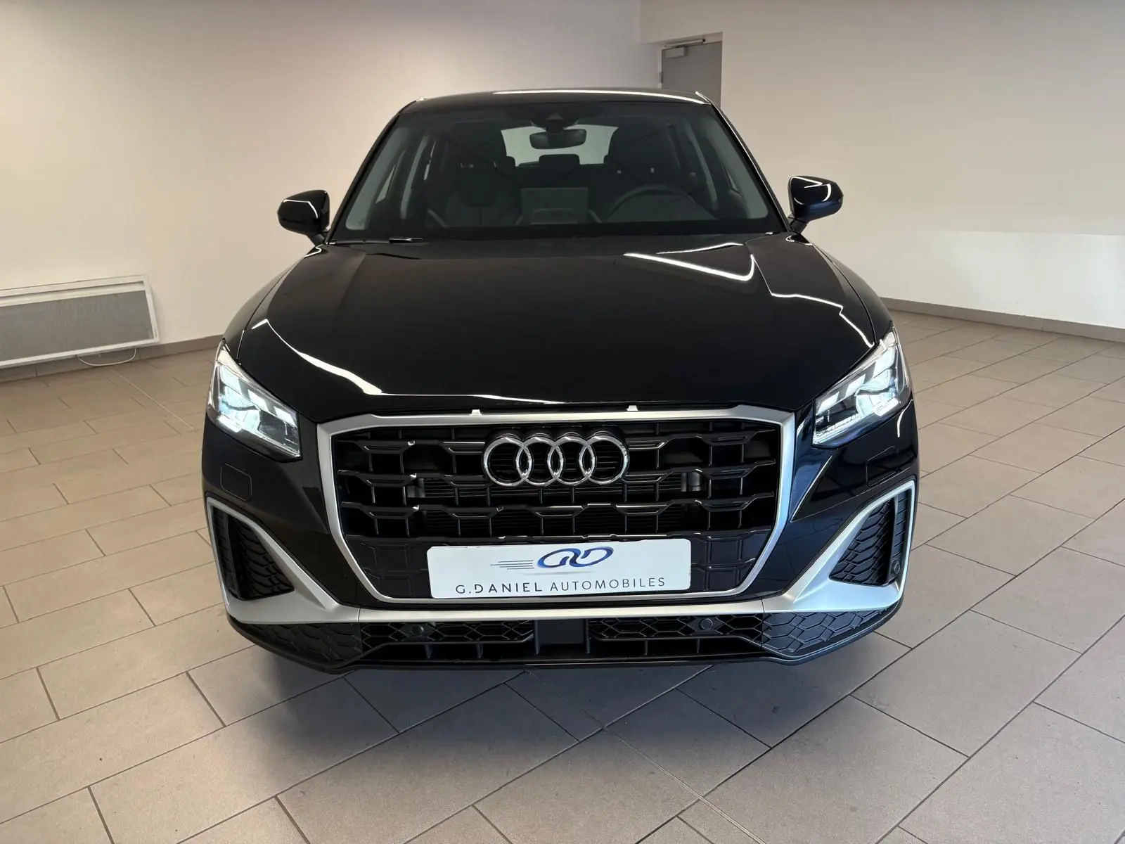 Vue avant d'un Audi Q2 35 TFSI S Line noir mythic avec calandre large et phares LED allumés en intérieur showroom.