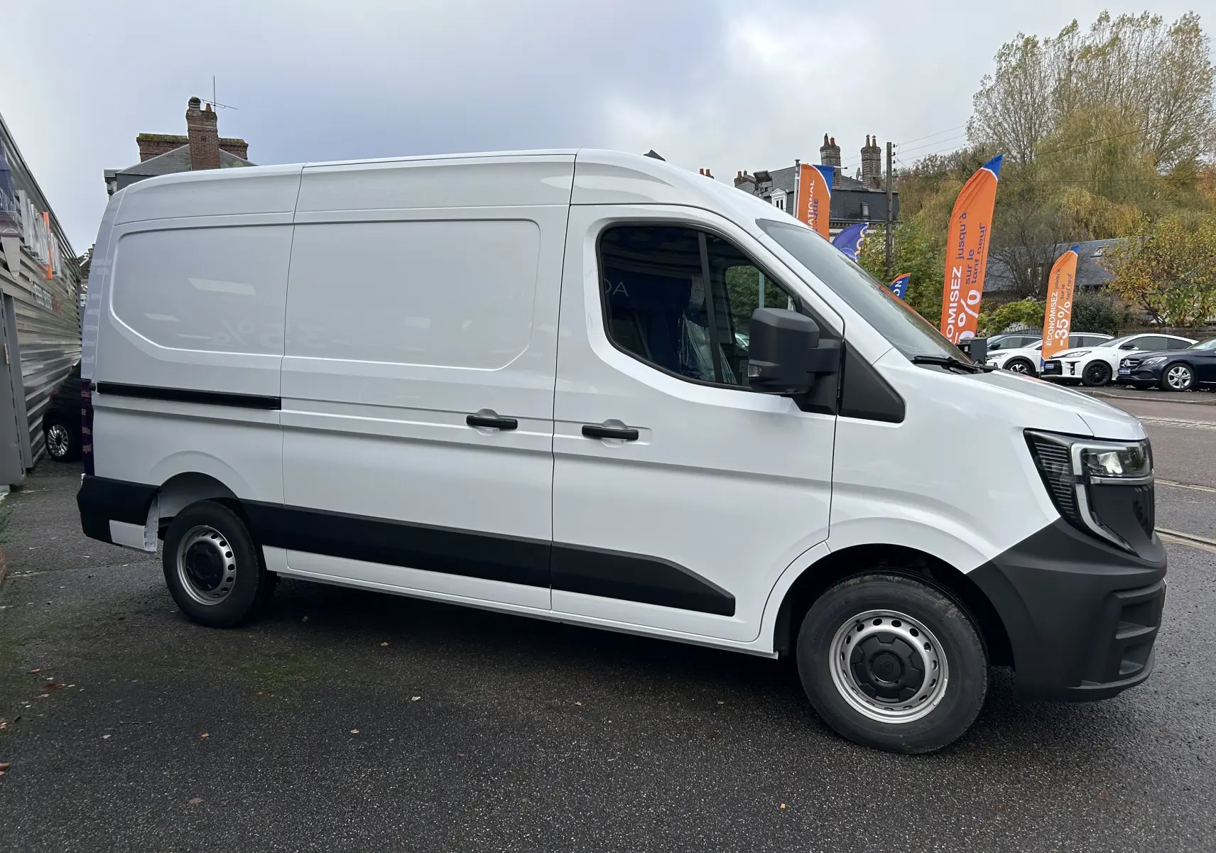 Vue de profil côté droit du fourgon Renault Master blanc, avec pare-chocs et bas de caisse noirs, stationné en extérieur.