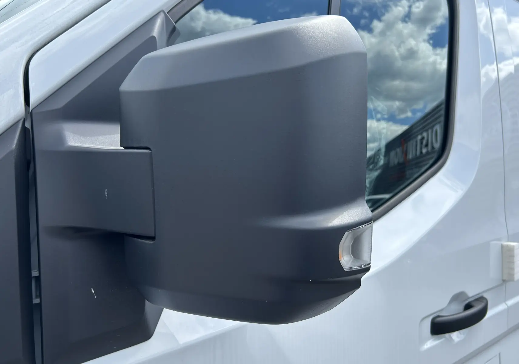 Gros plan sur le rétroviseur droit noir du Renault Master blanc, avec reflet du ciel et partie de la porte visible.