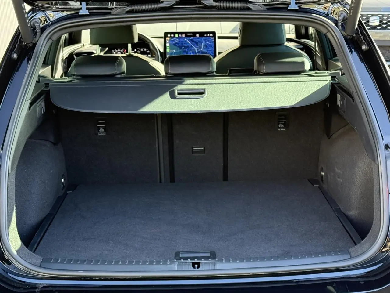 Coffre ouvert d'une CUPRA LEON ST noir Midnight, vue arrière montrant l'habitacle et l'écran tactile du tableau de bord.