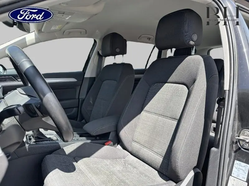 Vue intérieure côté conducteur de la Volkswagen Passat SW 2.0 TDI gris Manganese, sièges tissu noir avec volant cuir multifonction.