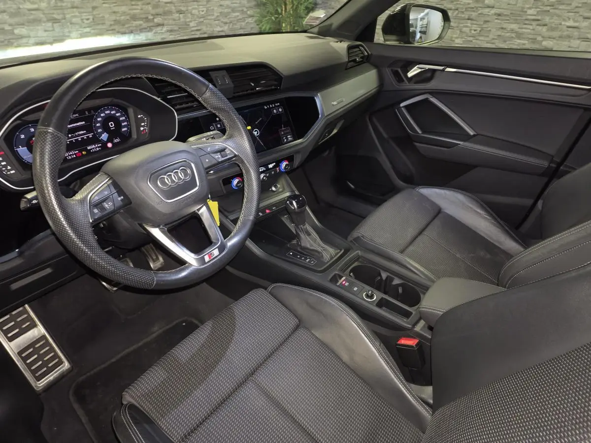 Vue intérieure côté conducteur de l'Audi Q3 Sportback 2023 noire, volant cuir S line et tableau de bord numérique.