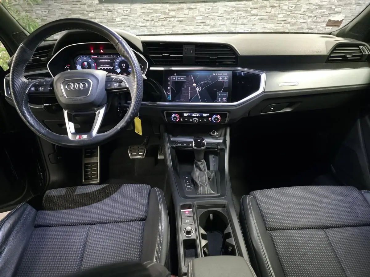 Vue intérieure avant de l'Audi Q3 Sportback noir, tableau de bord moderne avec écran tactile et volant multifonctions cuir.