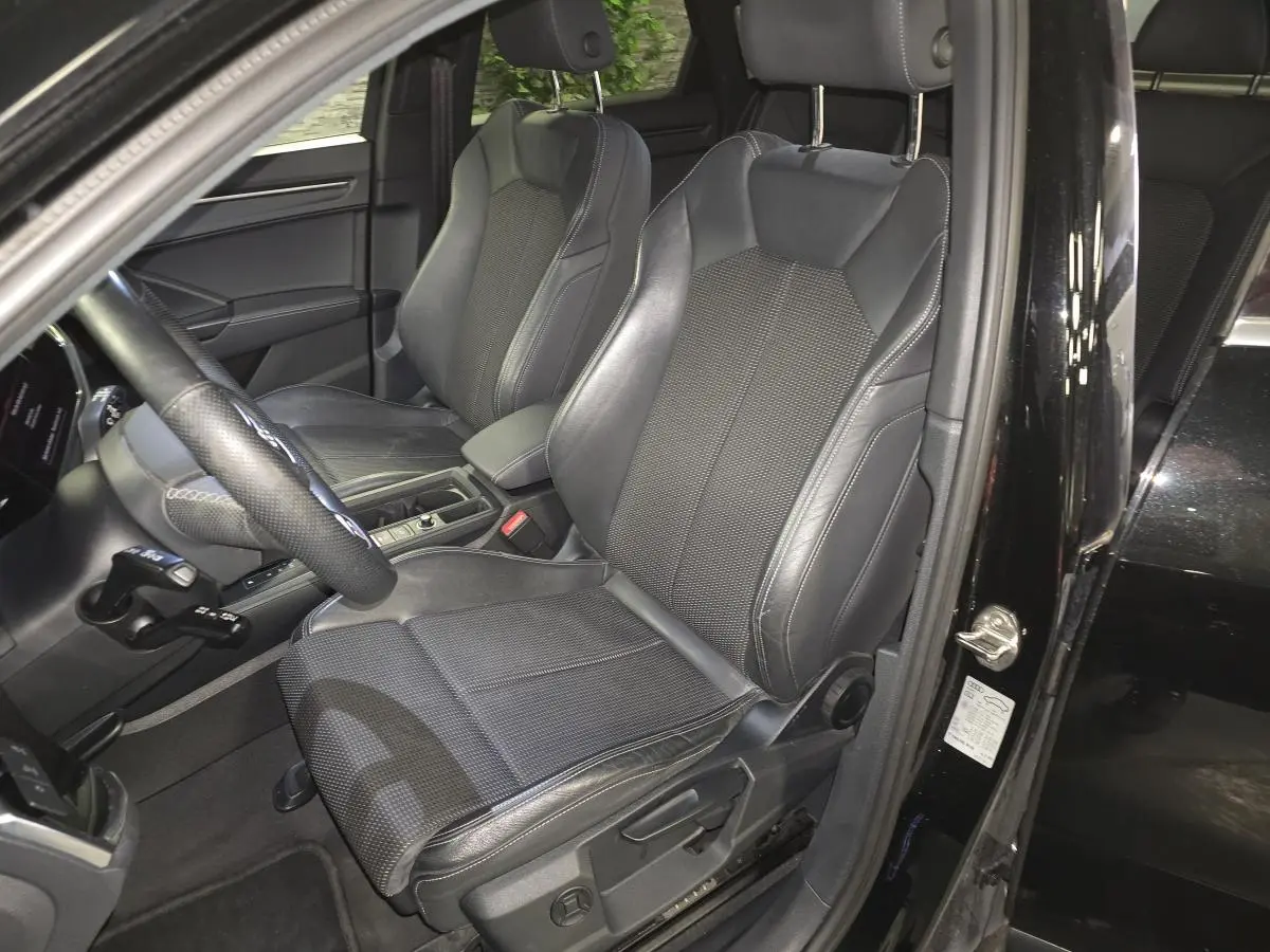 Vue intérieure côté conducteur de l'Audi Q3 Sportback noir 2023, sièges sport en cuir et tissu avec surpiqûres grises.