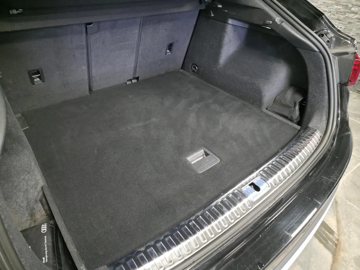 Coffre ouvert de l'Audi Q3 Sportback noir, vue en plongée montrant la surface et la protection en acier inoxydable du seuil.