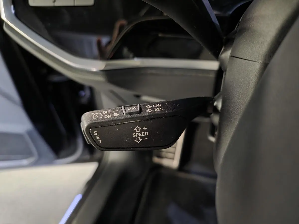 Gros plan sur la commande de régulateur de vitesse noire à gauche du volant dans l’Audi Q3 Sportback noir 2023.