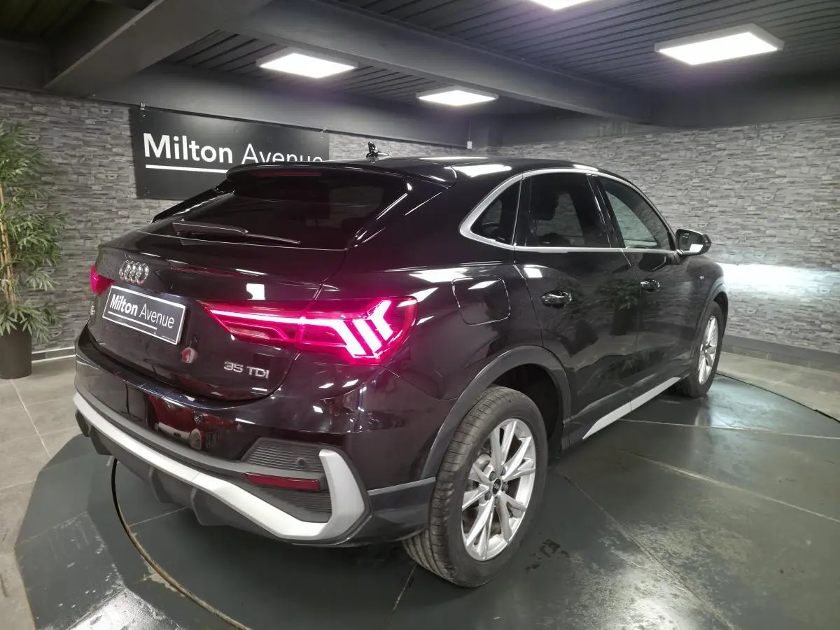 Audi Q3 Sportback noir vue 3/4 arrière droit, feux LED allumés et jantes aluminium 5 branches visibles.