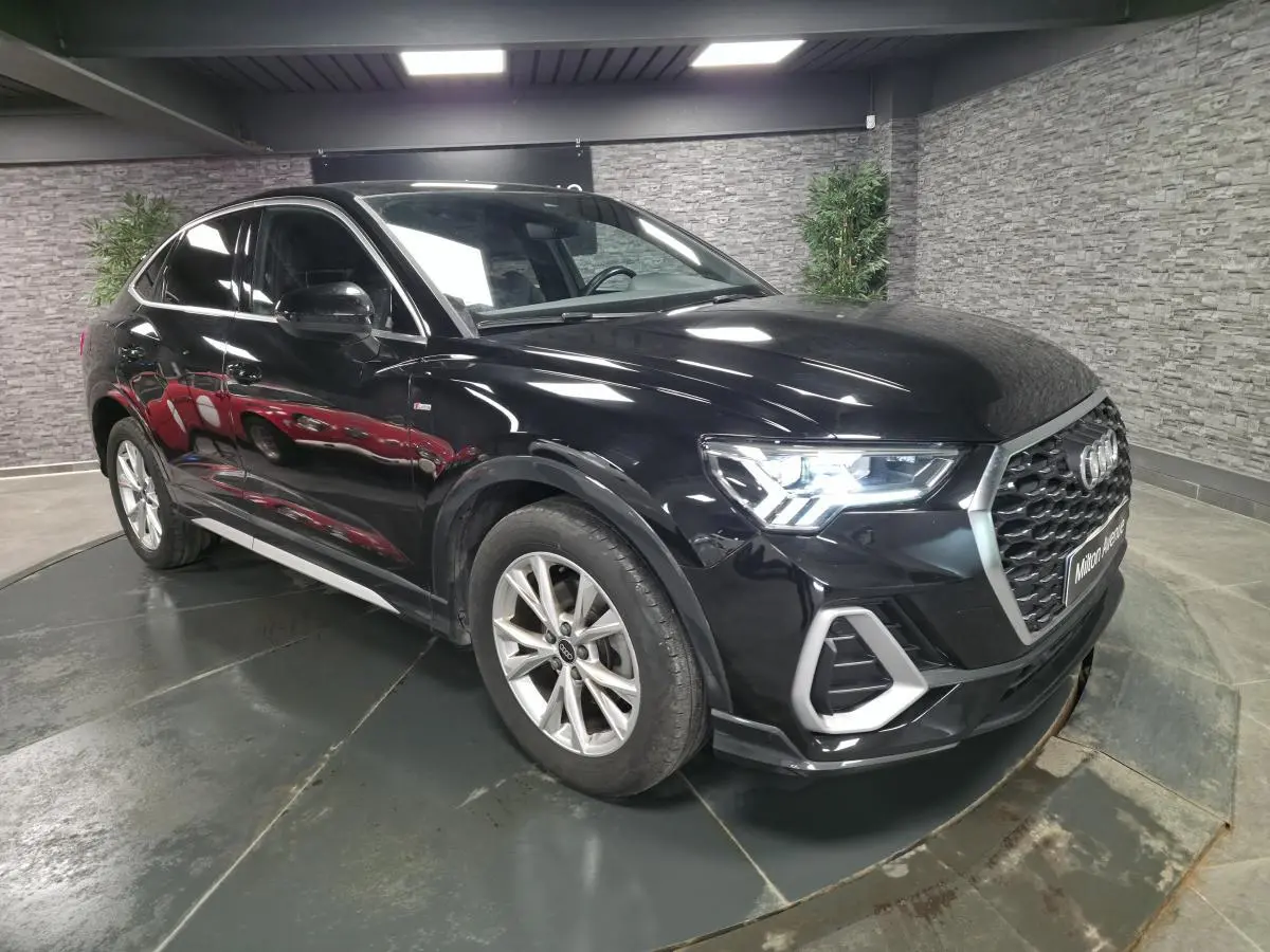 Audi Q3 Sportback noir vue 3/4 avant droit en intérieur, avec calandre hexagonale et jantes 5 branches.