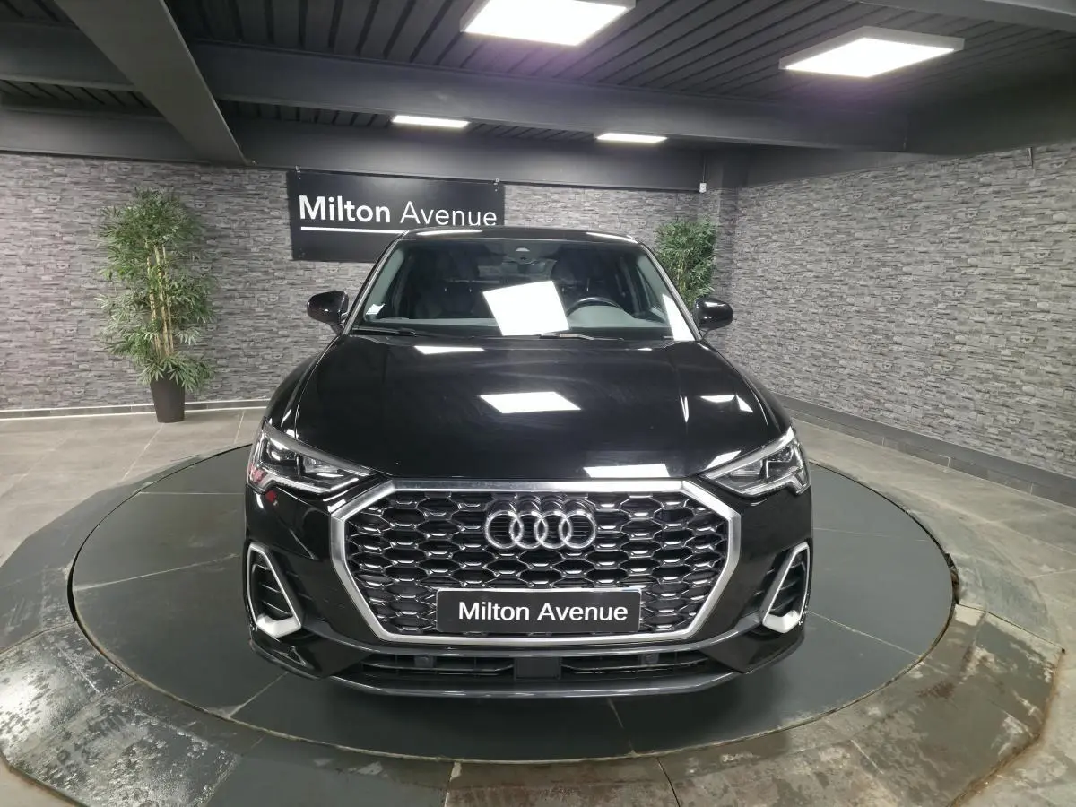 Audi Q3 Sportback noir vue de face en intérieur, calandre hexagonale et phares LED distinctifs visibles.