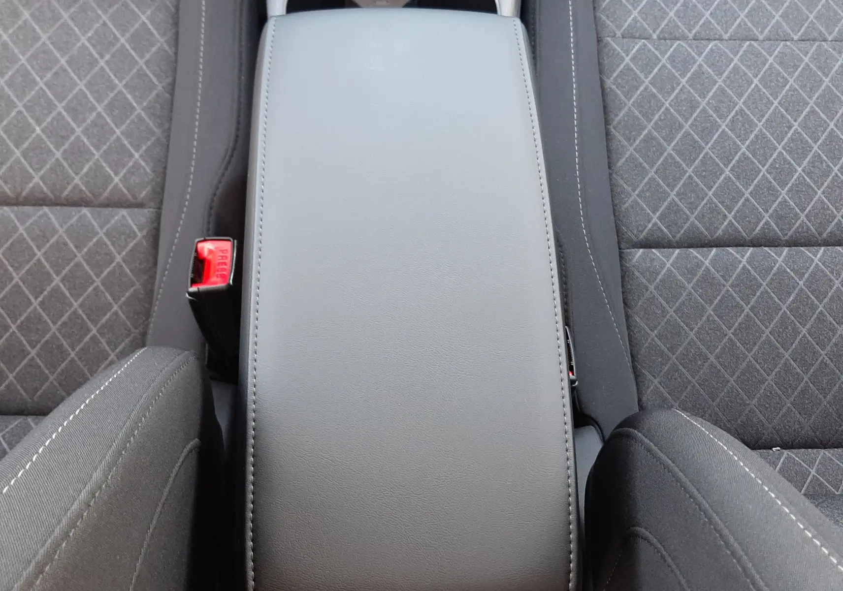Vue plongeante sur l'accoudoir central gris et les sièges tissu gris à motifs du MG Motor ZS 1.5 Hybrid+ 2026.