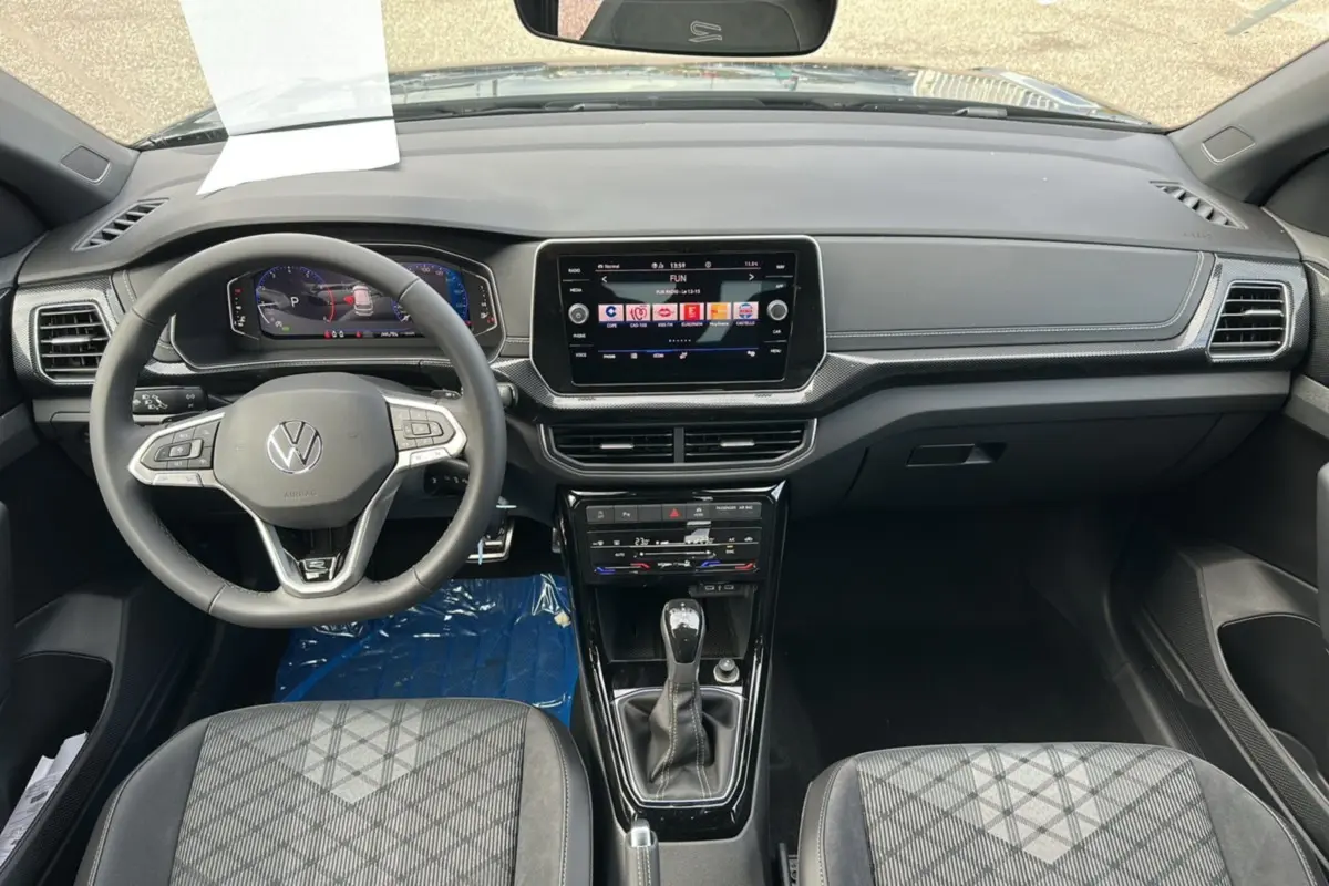 Vue intérieure avant du Volkswagen T-Cross TSI 116 DSG7 R-Line 2025 avec tableau de bord numérique et sièges tissu gris.