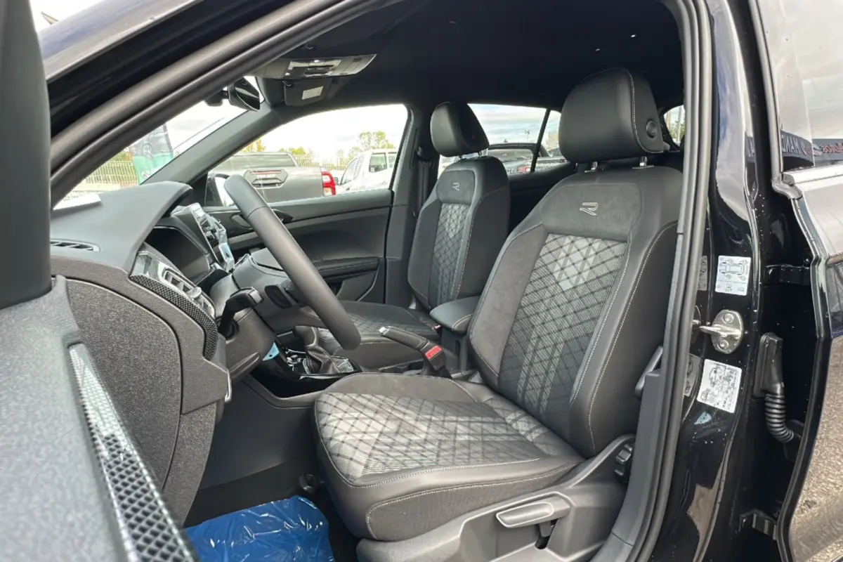 Vue intérieure côté conducteur du Volkswagen T-Cross TSI 116 DSG7 R-Line 2025 avec sièges tissu noirs et logo R brodé.