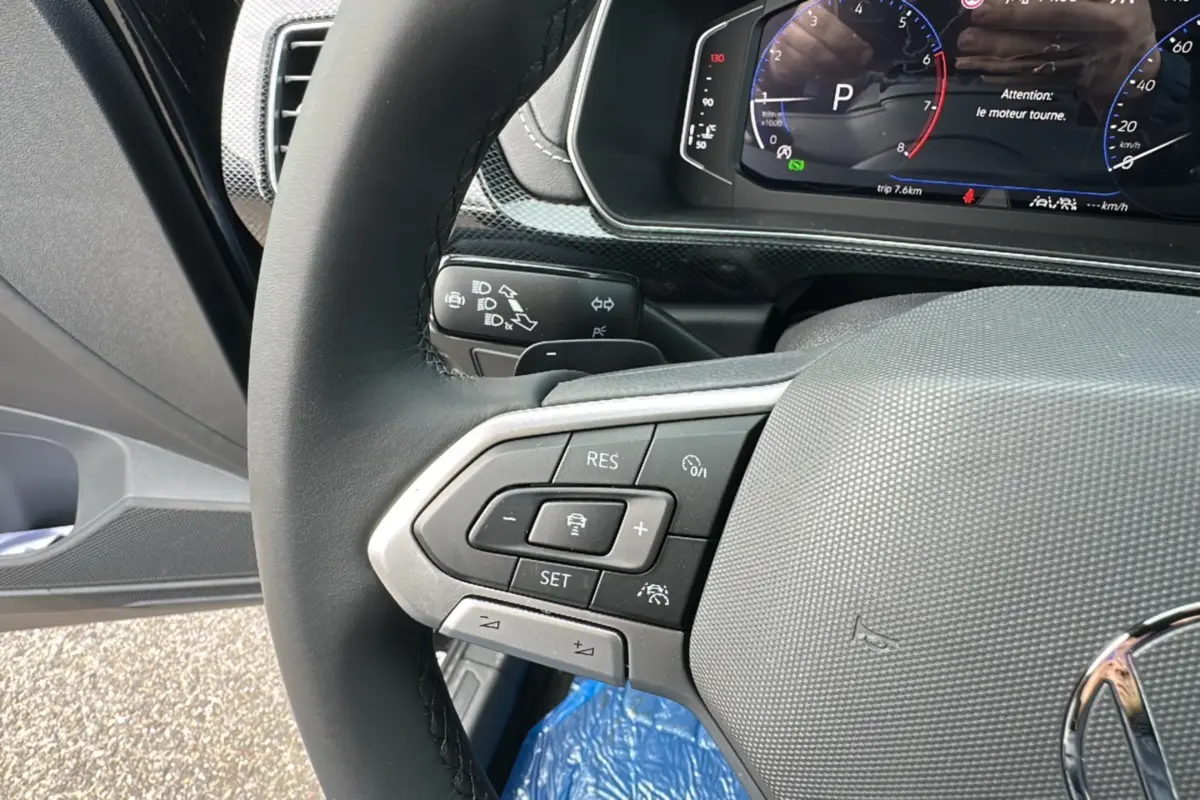 Gros plan sur le volant cuir multifonctions du Volkswagen T-Cross noir intense 2025, affichage digital en arrière-plan.