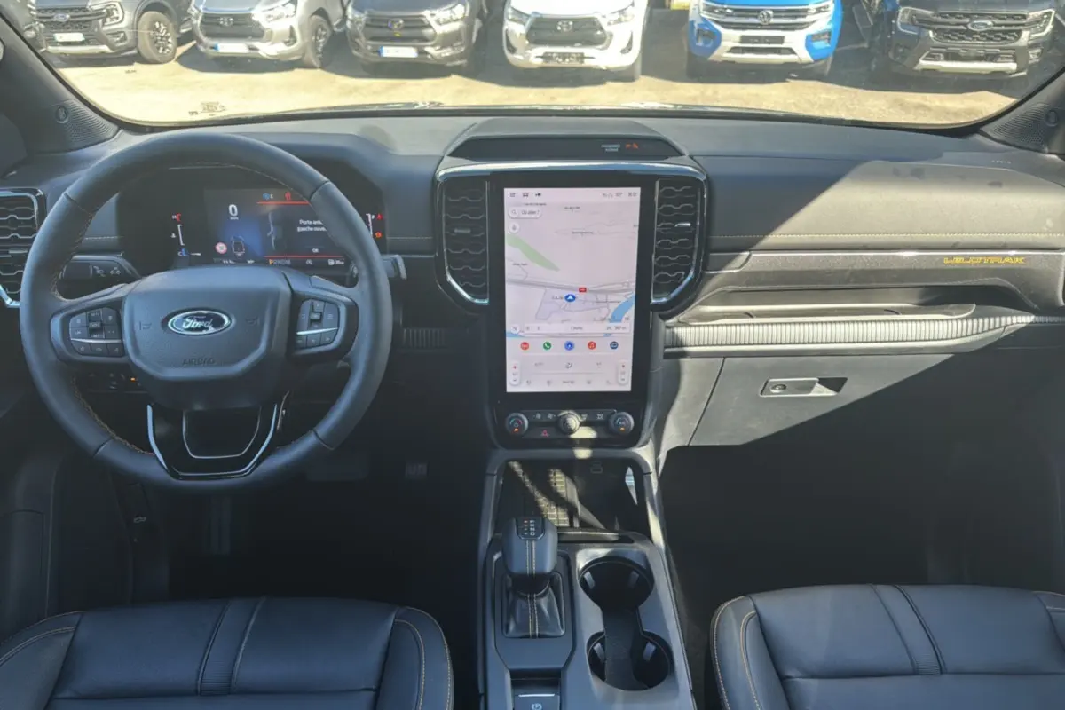 Vue intérieure frontale du Ford Ranger Wildtrak 2025 avec tableau de bord noir, écran tactile vertical et volant multifonctions.