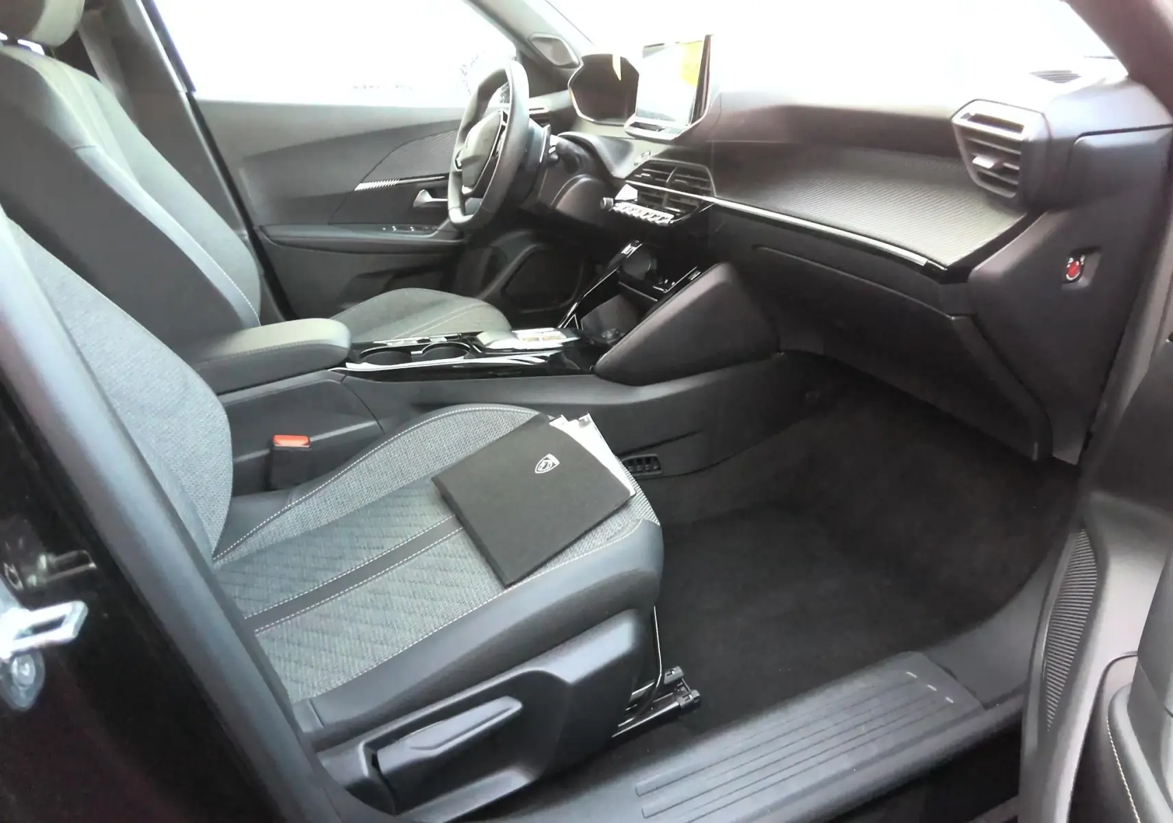 Vue intérieure côté conducteur du Peugeot 2008 noir 2025, montrant sièges tissu et tableau de bord moderne avec écran tactile.