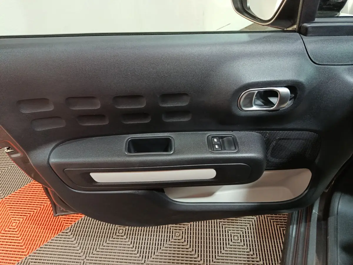 Vue intérieure côté gauche de la porte avant d'une Citroën C3 gris foncé, avec commandes de vitres et poignée argentée.