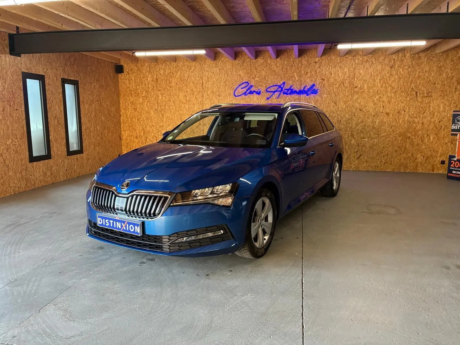 Vue 3/4 avant droite d'une Skoda Superb Combi bleu métallisé dans un showroom avec éclairage intérieur et mur en bois.