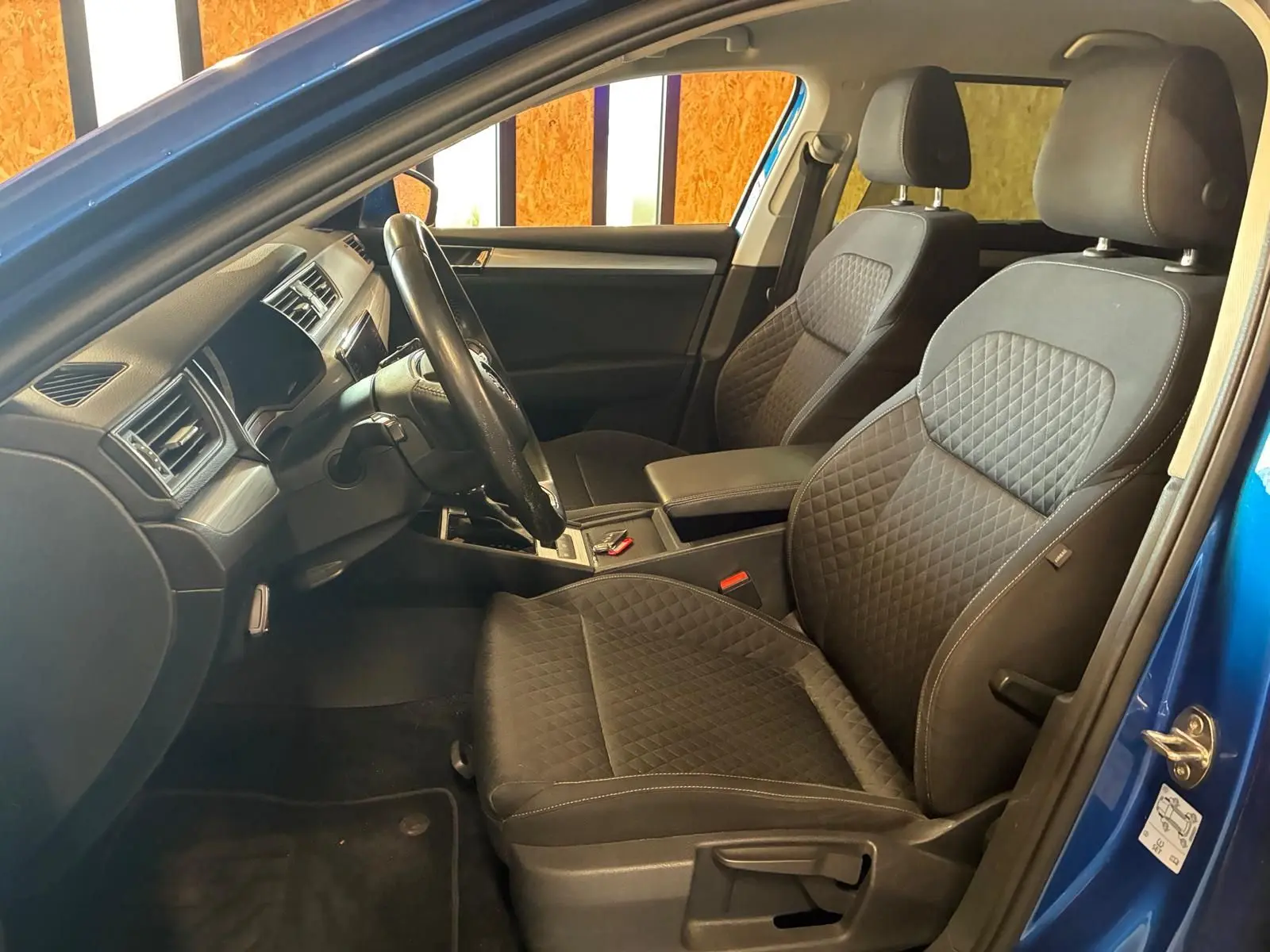 Vue intérieure côté conducteur d'une Skoda Superb Combi bleu 2021, sièges tissu noir avec surpiqûres et tableau de bord moderne.