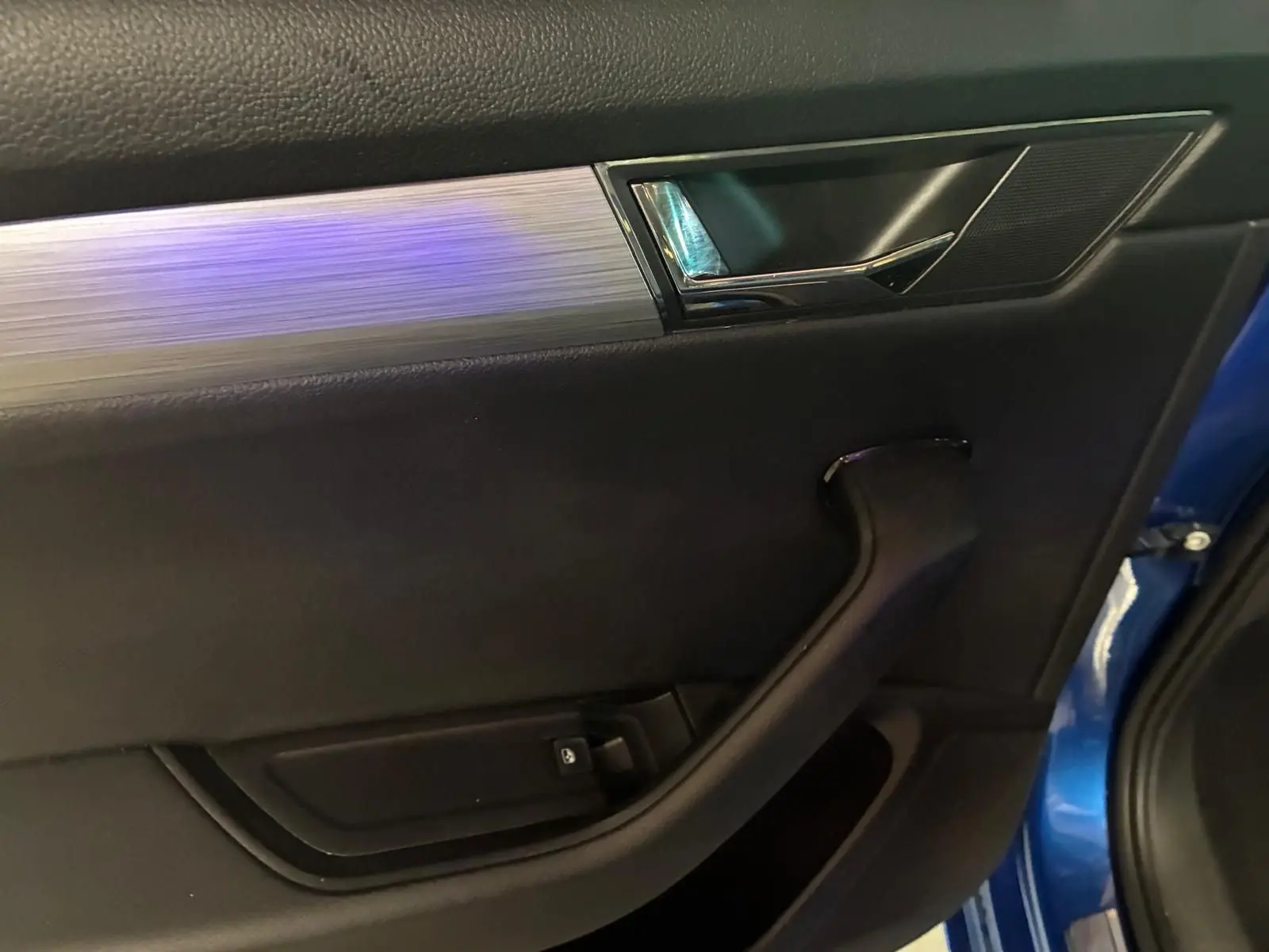 Détail de la porte intérieure côté gauche de la Skoda Superb Combi 2021 bleu, avec poignée noire et insert argenté.