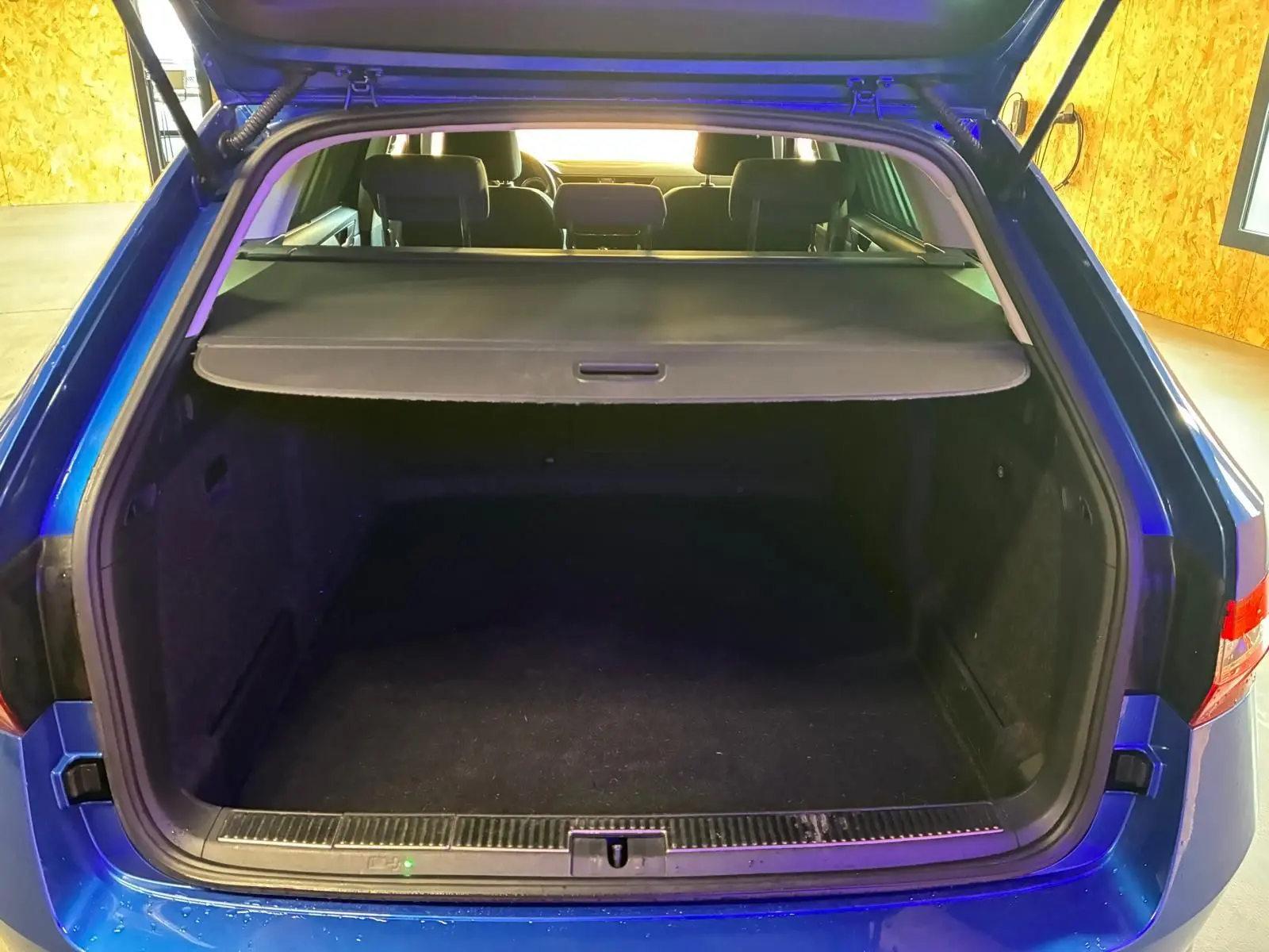 Coffre ouvert vu de l'arrière d'une Skoda Superb Combi bleu 2021, montrant l'espace de chargement et la tablette cache-bagages.