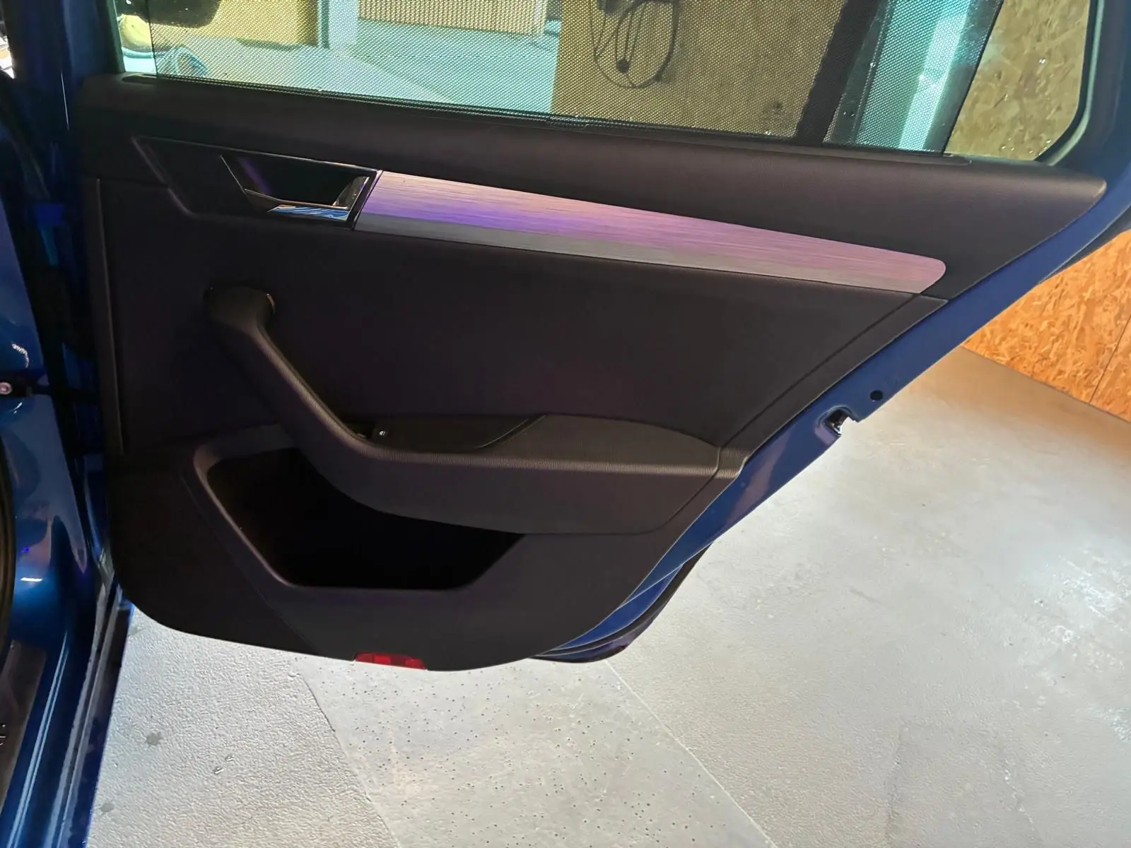 Gros plan sur la porte arrière gauche ouverte d'une Skoda Superb Combi bleu, avec garniture intérieure noire et insert argenté.