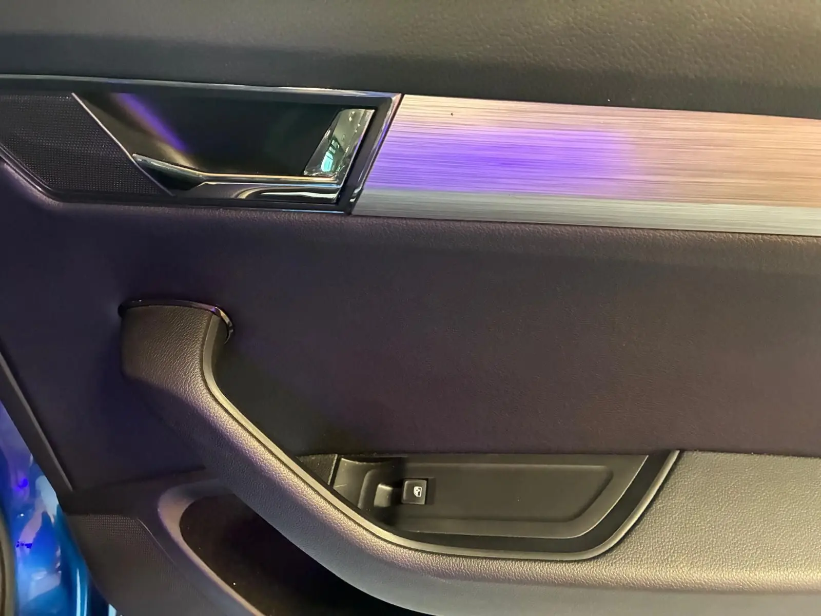 Intérieur côté gauche de la porte d’une Skoda Superb Combi bleu, avec poignée noire et insert aluminium brossé.