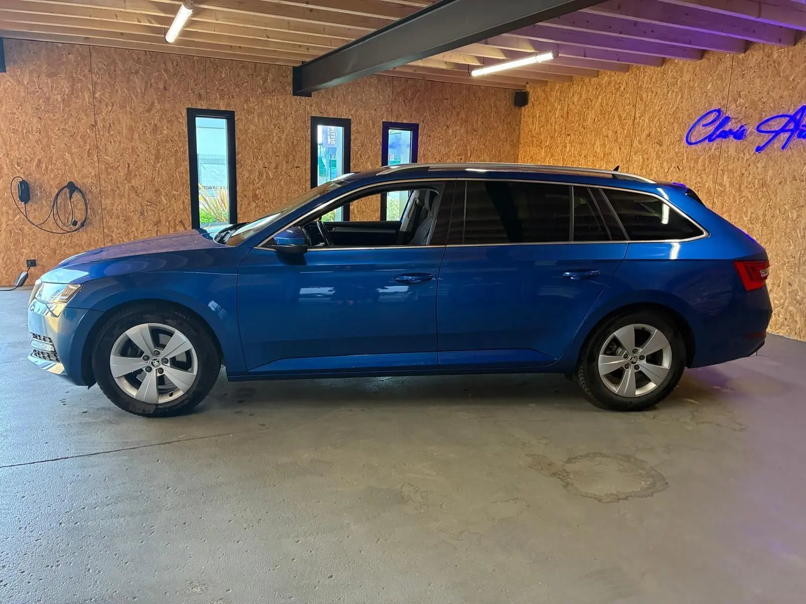 Vue latérale gauche d'une Skoda Superb Combi bleu 2021 stationnée en intérieur avec jantes alliage et vitres teintées.