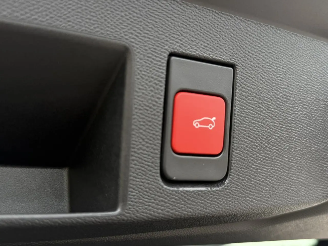Bouton rouge de hayon électrique sur panneau intérieur noir texturé du Citroën C5 Aircross blanc et noir.