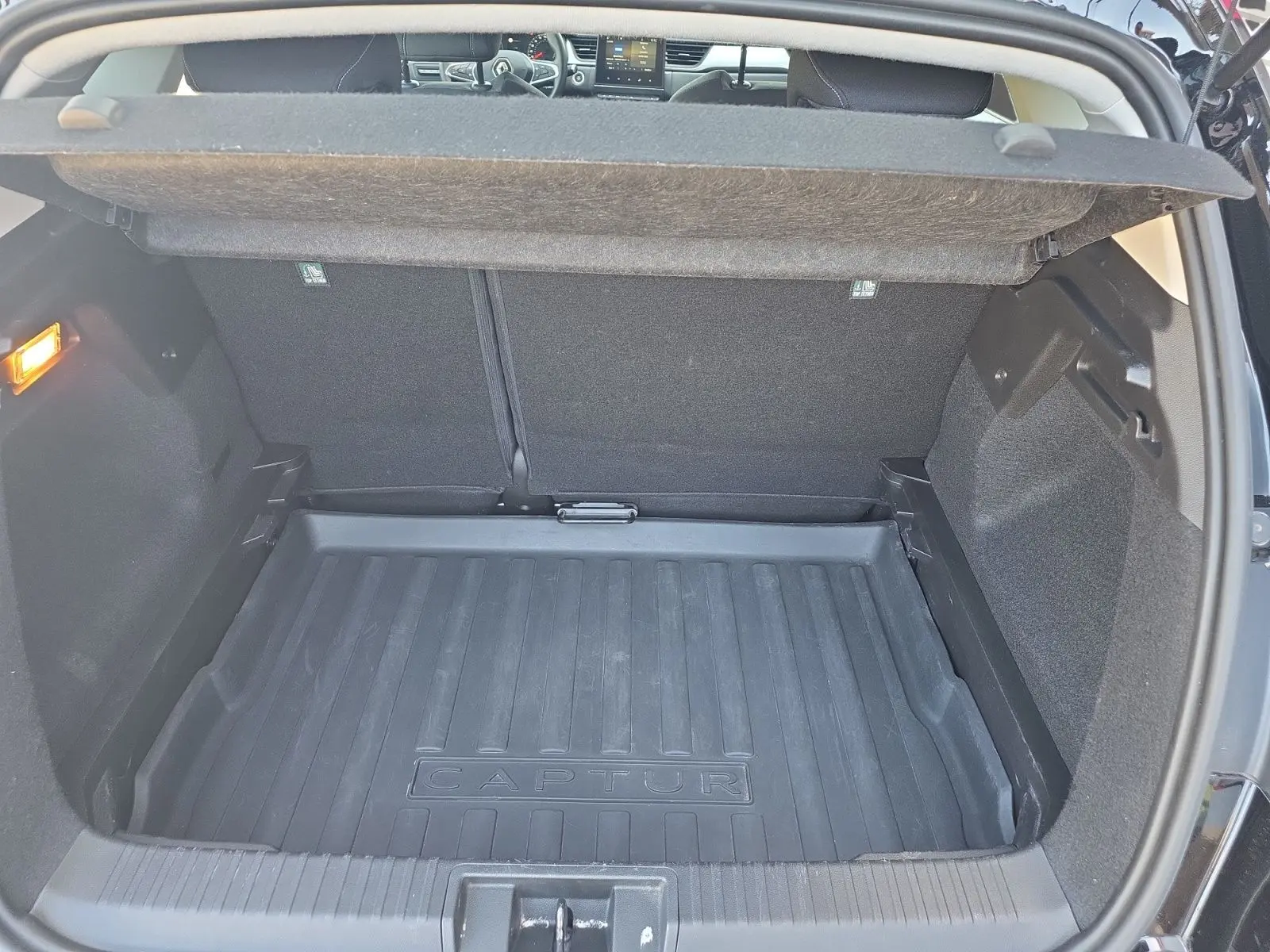 Coffre ouvert vu de l'arrière d'un Renault Captur noir, avec tapis de coffre marqué "CAPTUR" et intérieur sombre.