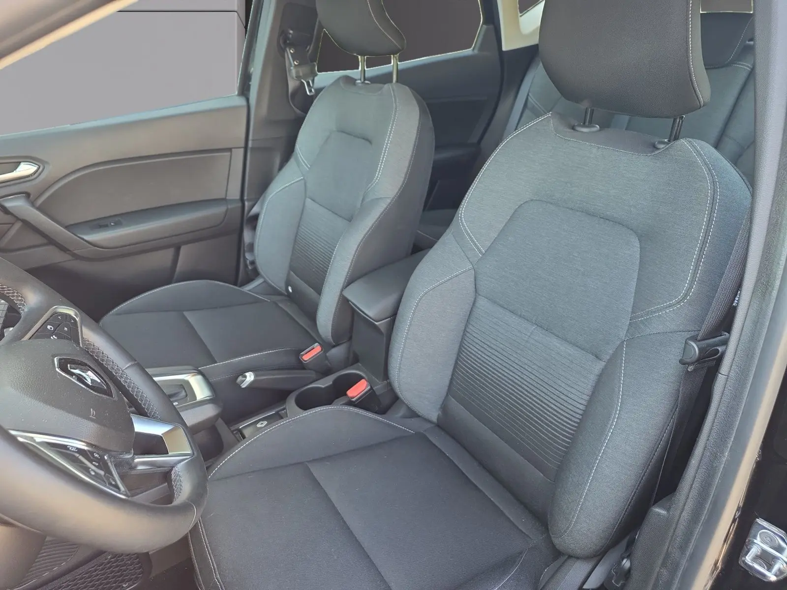 Vue intérieure rapprochée des sièges avant gris du Renault Captur noir, avec volant et accoudoir visibles côté gauche.