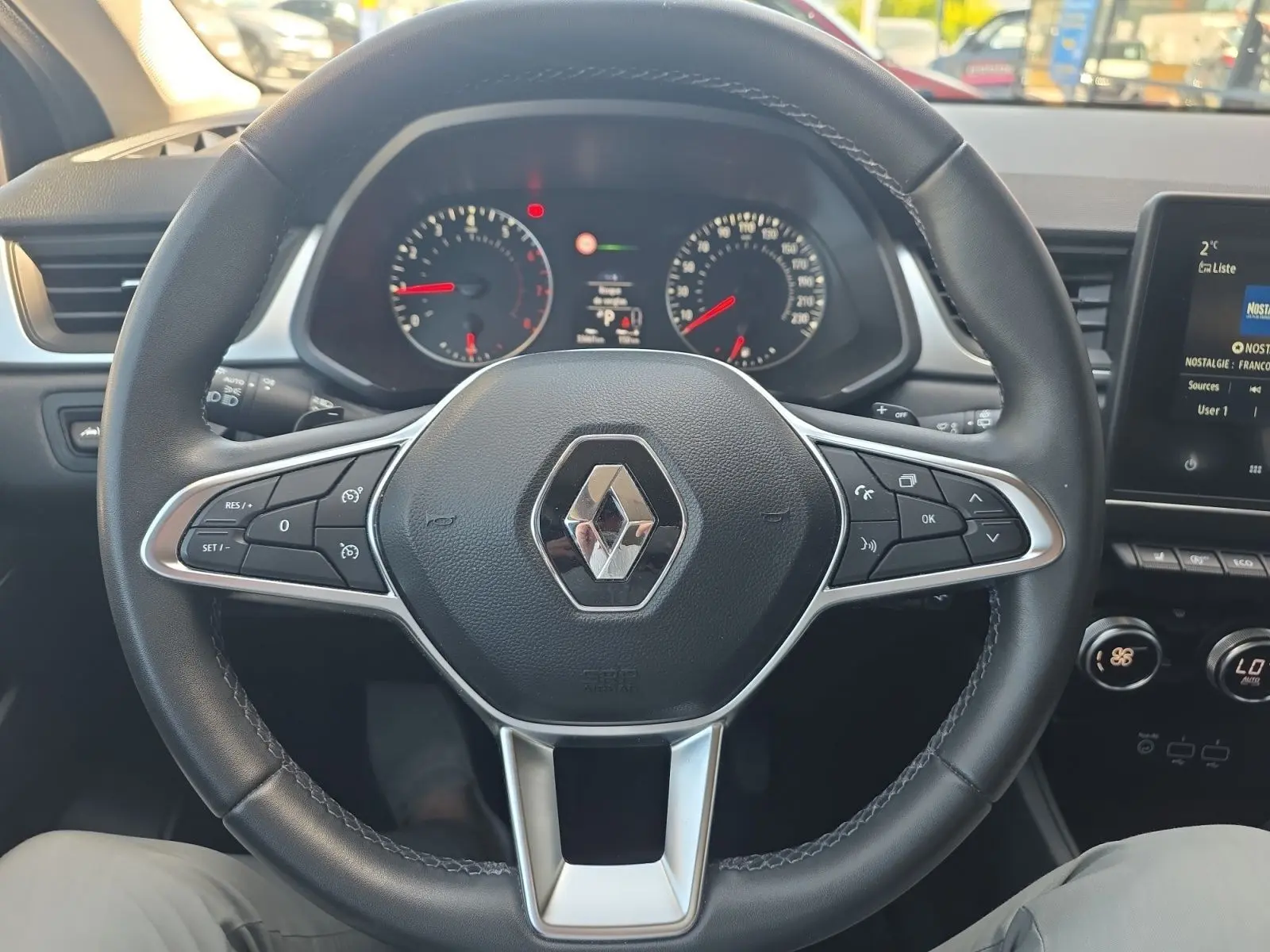Vue centrée du volant noir de Renault Captur 2021 avec commandes intégrées et tableau de bord en arrière-plan.