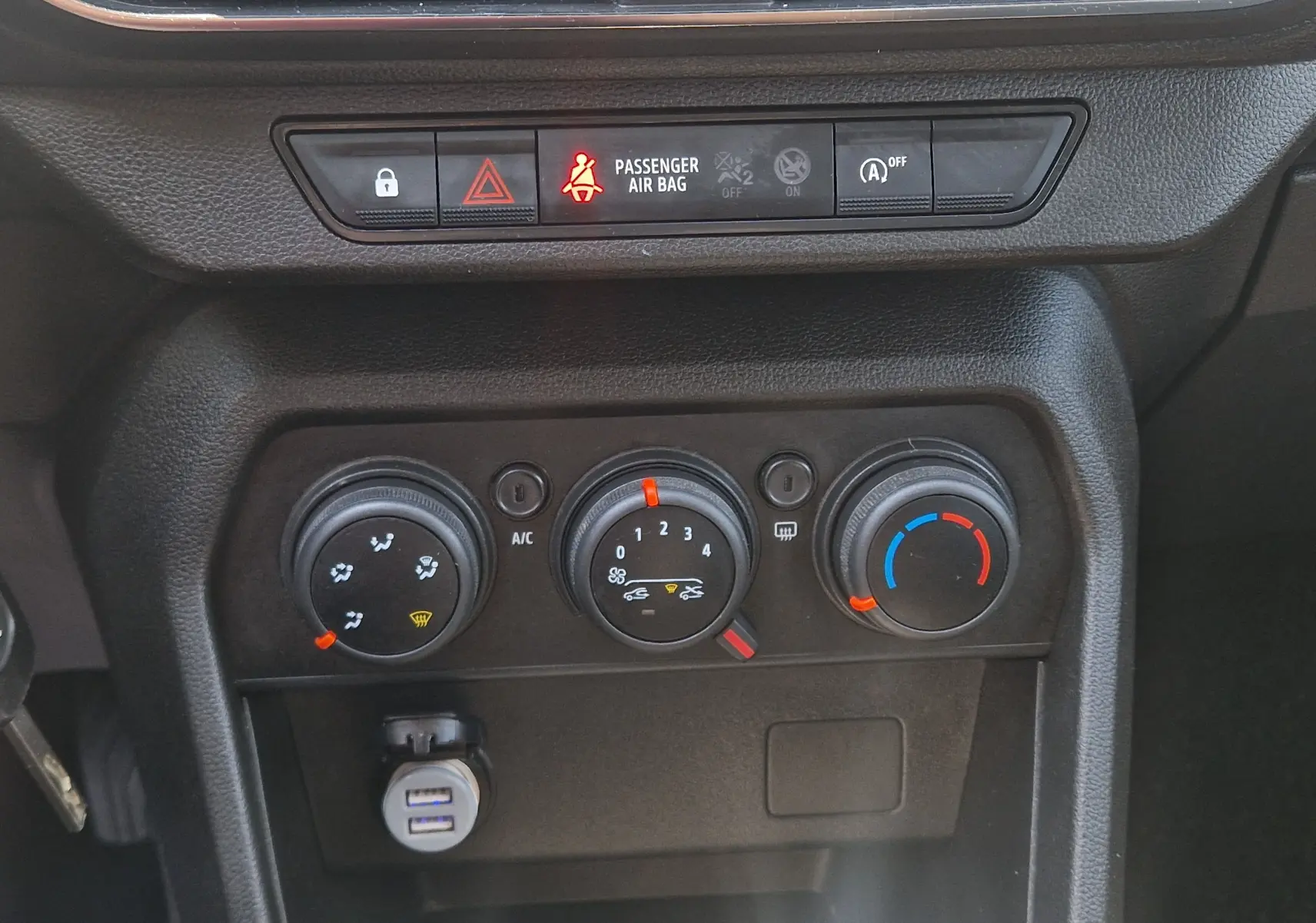 Vue rapprochée du tableau de bord de la Dacia Sandero blanche 2022, montrant les commandes de climatisation manuelle et les voyants lumineux.