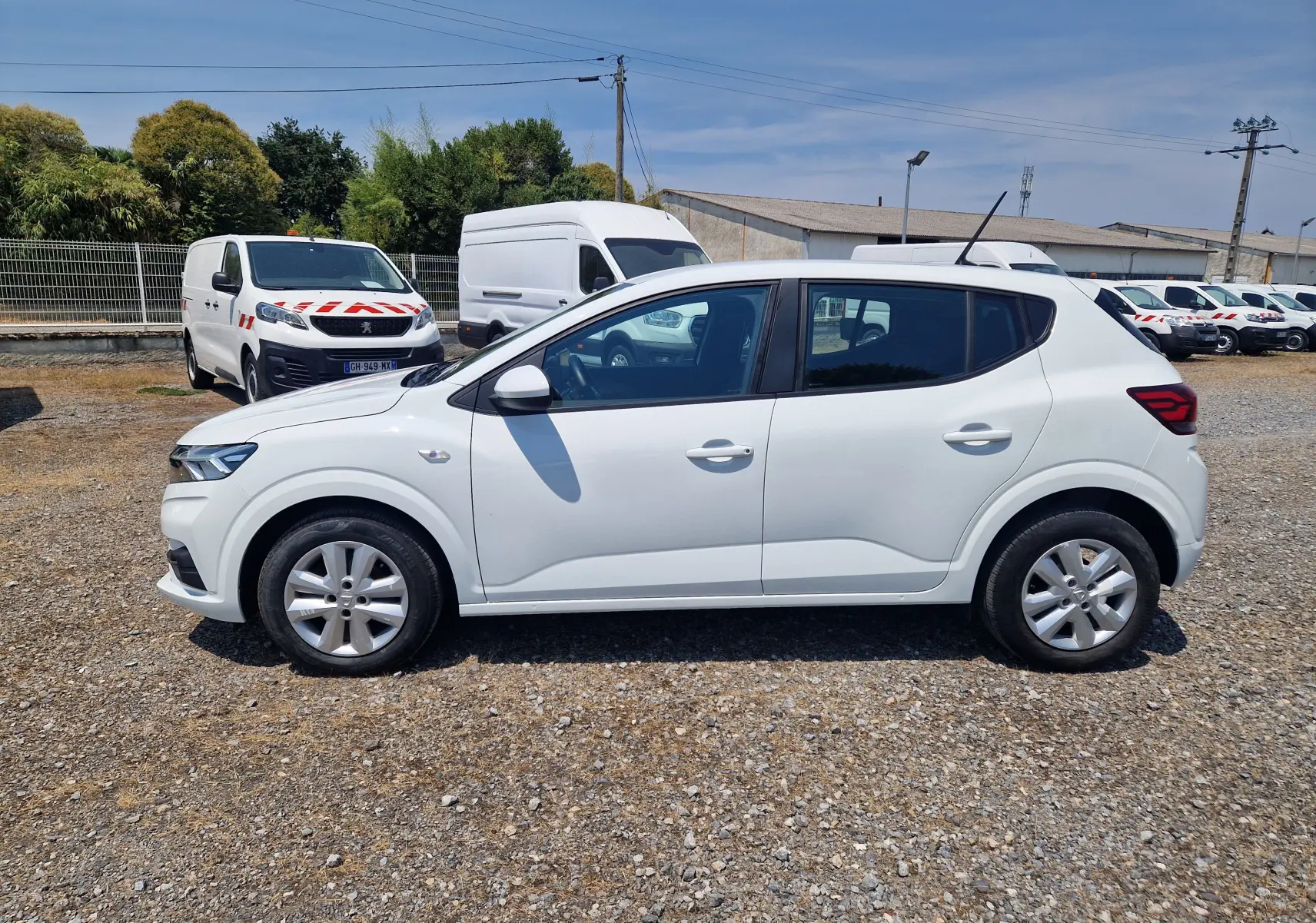 Vue latérale droite d'une Dacia Sandero blanche 2022, finition Confort, garée sur un sol gravillonné en extérieur.