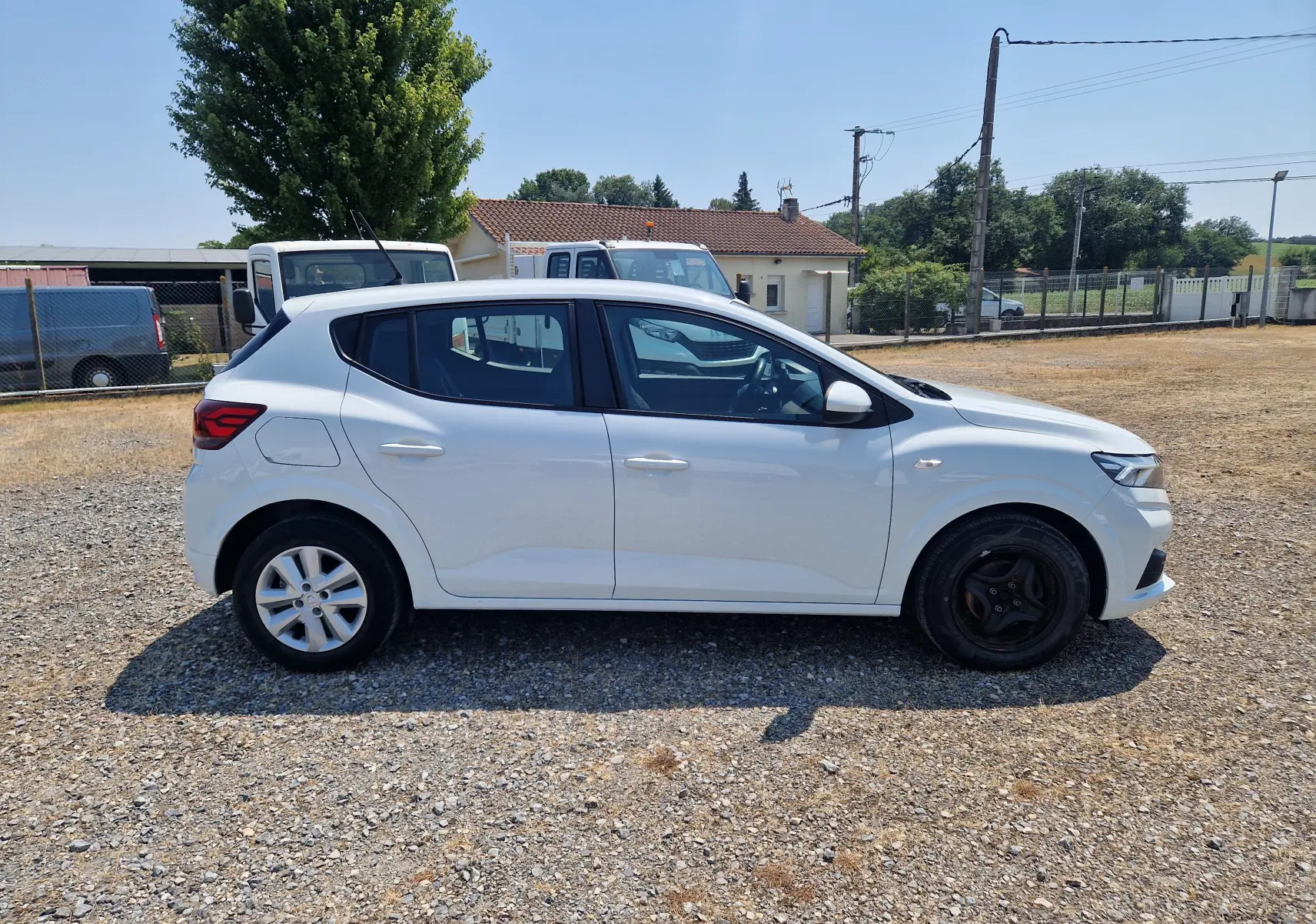 Vue de profil côté gauche d'une Dacia Sandero blanche 2022 SCE 65 - 22 Confort avec jantes différentes à l'avant et arrière.