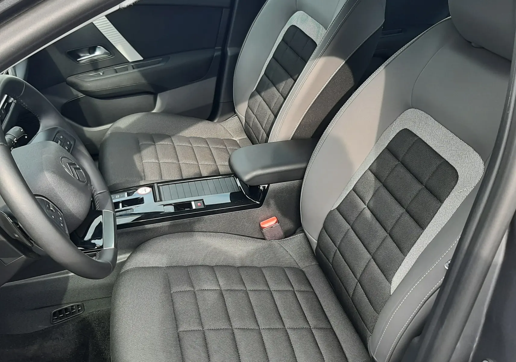 Vue intérieure côté conducteur de la Citroën C4 Hybrid 145ch Plus 2025, sièges tissu gris noir avec accoudoir central.