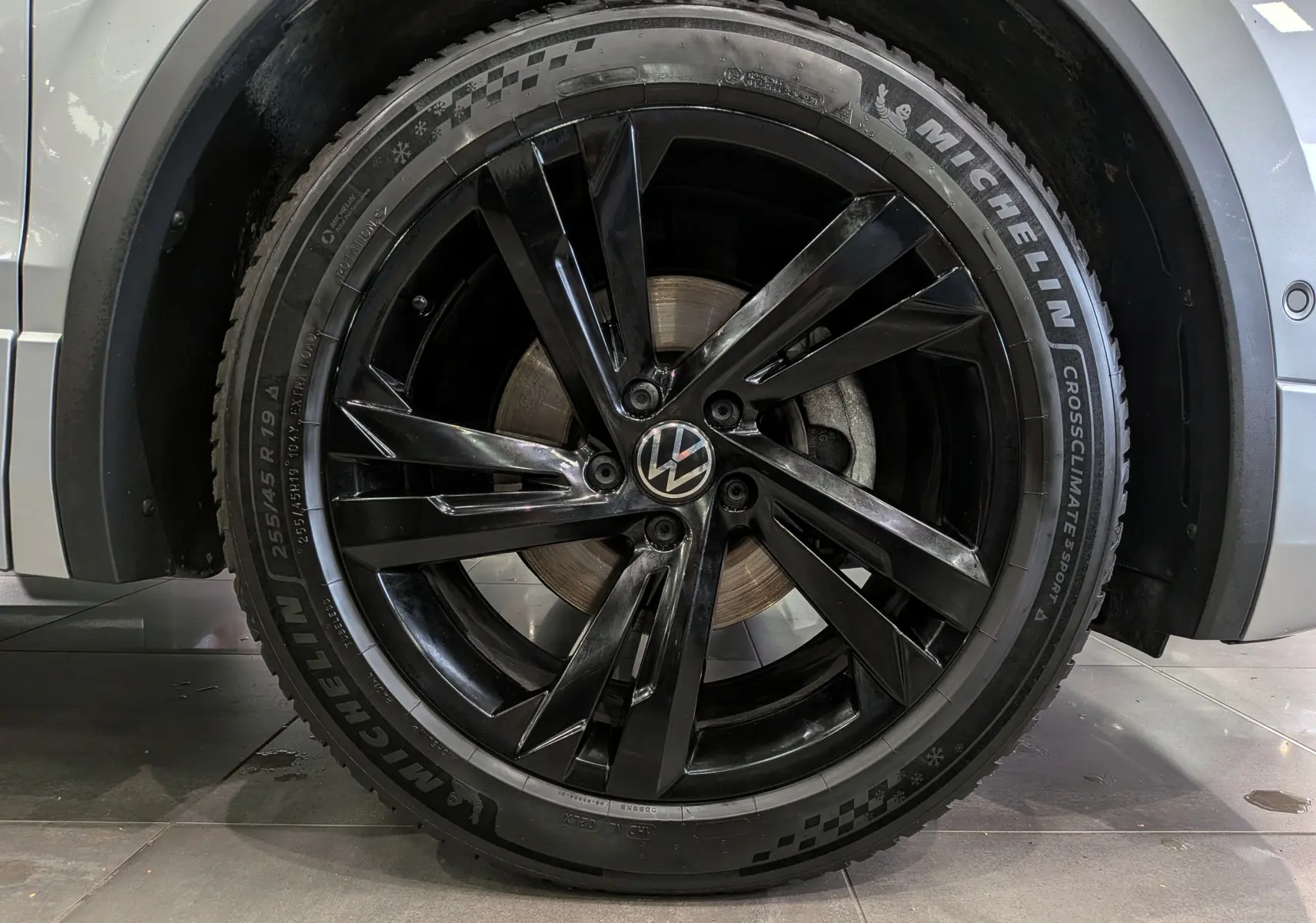 Gros plan sur la jante noire brillante de 19 pouces avec logo VW, montée sur un Volkswagen Tiguan reflet d'argent.